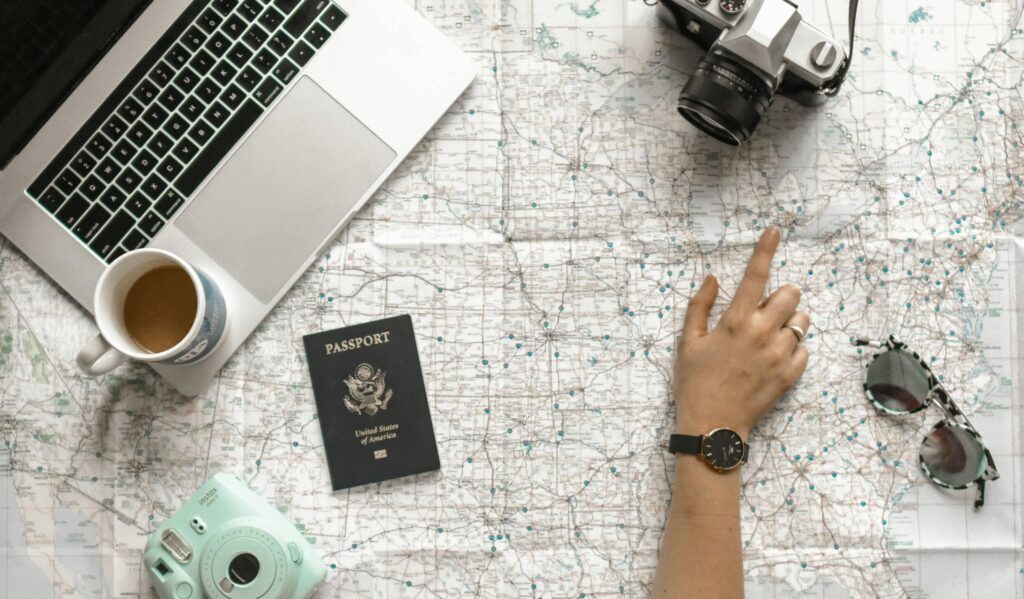 travel planning photo Hand on map with camera, passport, laptop, and coffee, perfect for travel planning inspiration.