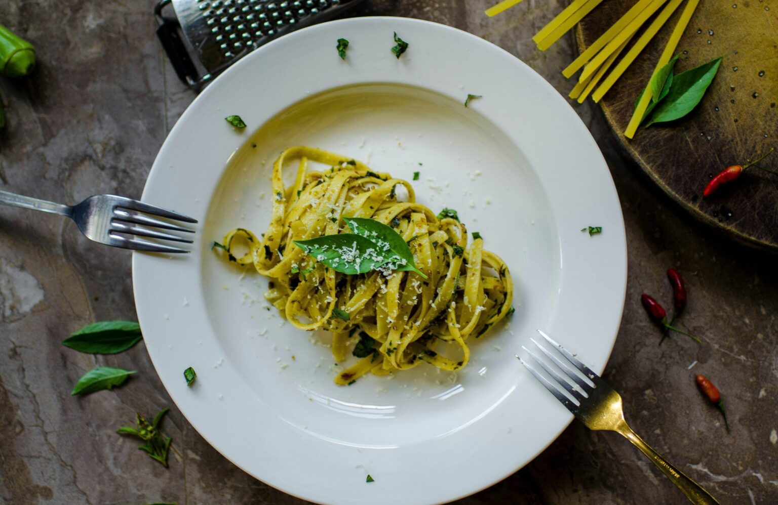A tempting plate of basil pesto pasta garnished with cheese, surrounded by fresh ingredients.